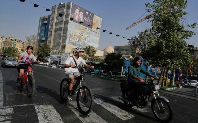 Un homme roulant à moto tandis que des garçons font du vélo, dans le centre-ville de Téhéran, en Iran, le 22 juillet 2026. (Crédit : Vahid Salemi/AP)