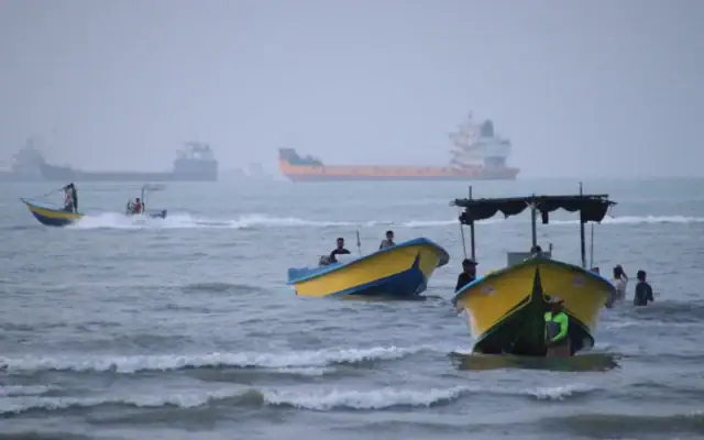 De petites embarcations longent le rivage tandis que des cargos et d’autres navires marchands sont ancrés dans le détroit d’Ormuz, au large de Bandar Abbas, en Iran, le 27 juillet 2026. (Crédit : Razieh Poudat/ISNA via AP)