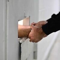 Un gardien menottant les mains d'un prisonnier, à la prison de Givon, à Ramle, le 11 janvier 2026. (Crédit : Oren Cohen/Flash90)