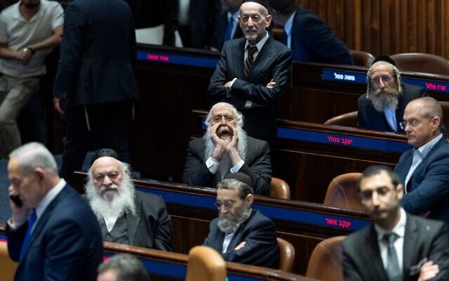 Le Premier ministre Benjamin Netanyahu (au premier plan) passe devant des députés ultra-orthodoxes alors que la Knesset s'apprête à adopter une loi interdisant l'arrestation des réfractaires au service militaire, ce qui aura pour effet de geler l'enrôlement des ultra-orthodoxes dans l'armée israélienne pendant au moins les sept prochains mois, le 14 juillet 2026. Netanyahu a quitté l'assemblée avant le vote proprement dit. (Crédit : Chaim Goldberg/Flash90)