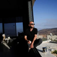 Le Palestinien-Américain Loui Abu Ridi regarde par la fenêtre de sa maison, encerclée par des résidents d’implantations depuis plus d’une semaine, après avoir pu y accéder, à Qusra, en Cisjordanie, le 18 août 2026. (Crédit : Ammar Awad/Reuters)