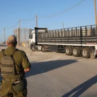 Un officier israélien observe des camions chargés d’aide humanitaire en provenance de Jordanie entrer à Gaza par le poste-frontière d’Erez, contrôlé par Israël, à la frontière avec le nord de la bande de Gaza, le 21 octobre 2024. (Crédit : Jack Guez/AFP)