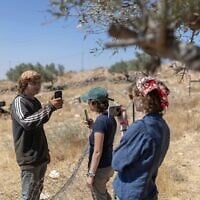 Des militants de l’organisation « Protective Presence » (à droite) faisant face à un résident d'implantation qui les filme également avec son téléphone portable, alors qu’il tente de pénétrer dans la maison d’une famille bédouine en Cisjordanie, à l’est de Ramallah, juste à la sortie du village de Taybeh, le 22 juin 2026. (Crédit : Ilia Yefimovich/AFP)
