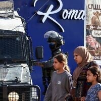 Des Palestiniens passent devant les forces de sécurité israéliennes déployées dans une rue lors d'une opération militaire dans le camp de réfugiés de Qalandiya, au sud de Ramallah en Cisjordanie, le 5 août 2026. (Zain JAAFAR/AFP)