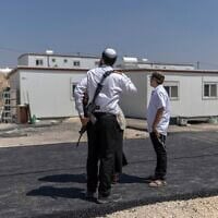 Des résidents d'implantations israéliens se tiennent devant des maisons après la réouverture de l'implantation de Ganim, en Cisjordanie, le 13 août 2026. (Crédit : Ilia Yefimovitch/AFP)
