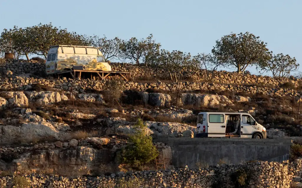 Des véhicules utilisés par des partisans du mouvement pro-implantations dans le village de Qusra, en Cisjordanie, devant les maisons qu'ils assiègent dans le village, le 18 août 2026. (Crédit : Ilia YEFIMOVICH/AFP)