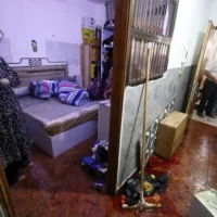 La femme de Fathi Khazem, 58 ans, tué alors qu'il tentait de poignarder un soldat lors d'une interpellation, se tient devant la porte de sa chambre près d'une flaque de son sang au domicile familial à Jénine, dans le nord de la Cisjordanie, le 21 août 2026. (Jaafar Ashtiyeh/AFP)