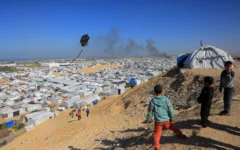 Des jeunes garçons font voler un cerf-volant avec, en arrière-plan, la fumée s'élevant du centre d'accueil de Gath, qui héberge des Palestiniens déplacés, après une frappe aérienne israélienne à l'ouest de Khan Younis, dans le sud de la bande de Gaza, le 31 janvier 2026. (Crédit: Bashar Taleb/AFP)