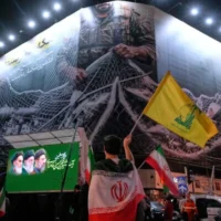 Un manifestant drapé dans une bannière iranienne brandit le drapeau du Hezbollah, le groupe relais de l'Iran au Liban, devant un panneau d'affichage représentant des avions américains tombant dans les filets des forces iraniennes, accompagné de la légende en persan : "Le détroit d'Ormuz restera fermé ; l'ensemble du golfe Persique est notre terrain de chasse", lors d'un rassemblement pro-gouvernement sur la place de la Révolution islamique à Téhéran, en Iran, le 4 mai 2026. (AP Photo/Vahid Salemi)