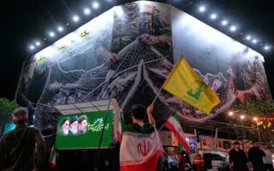 Un manifestant drapé dans une bannière iranienne brandit le drapeau du Hezbollah, le groupe relais de l'Iran au Liban, devant un panneau d'affichage représentant des avions américains tombant dans les filets des forces iraniennes, accompagné de la légende en persan : "Le détroit d'Ormuz restera fermé ; l'ensemble du golfe Persique est notre terrain de chasse", lors d'un rassemblement pro-gouvernement sur la place de la Révolution islamique à Téhéran, en Iran, le 4 mai 2026. (AP Photo/Vahid Salemi)