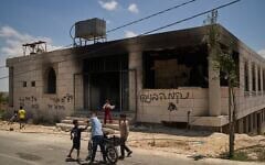 Des enfants se tiennent devant une mosquée incendiée lors d'une attaque menée par des résidents d'implantations israéliens tôt ce matin dans le village de Qusra, en Cisjordanie, le 26 juillet 2026. Sur le mur de l'édifice, un graffiti en hébreu indique « Vengeance Benayahu », en référence à un résident d'implantations israélien tué vendredi dernier lors d'affrontements avec des Palestiniens dans le village de Tell. (Crédit : AP Photo/Leo Correa)