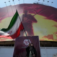 Une femme agitant un drapeau iranien sous un panneau d’affichage présentant une illustration appelant à la vengeance contre l’imam Hussein, l’un des saints les plus vénérés de l’islam chiite, et contre le défunt guide suprême iranien, l’ayatollah Ali Khamenei, sur une place du centre-ville de Téhéran, en Iran, le 1er août 2026. (Crédit : Vahid Salemi/AP)