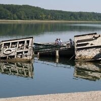 Des personnes observant l'épave d'un navire de guerre allemand de la Seconde Guerre mondiale, remise à nu par la sécheresse, devant le Djerdap II, un grand barrage sur le Danube, entre la Roumanie et la Serbie, près de Prahovo, en Serbie, le 4 août 2026. (Crédit : Darko Vojinovic/AP)