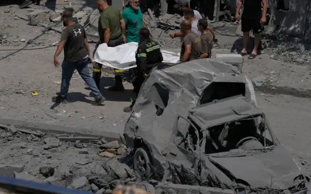 Des secouristes transportant le corps d'une personne tuée dans une maison touchée par une frappe aérienne israélienne à Deir al-Zahrani, dans le sud du Liban, le 15 août 2026. (Crédit : Mohammed Zaatari/AP)