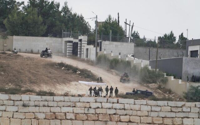 Des résidents d'implantations israéliens patrouillent sur une route devant des maisons palestiniennes assiégées, dans le village de Qusra, en Cisjordanie, au sud de Naplouse, le 17 août 2026. (Crédit : AP Photo/Majdi Mohammed)
