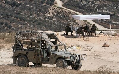 Des soldats de l'armée israélienne assis sous une tente devant la maison de Loui Abu Ridi, propriétaire palestinino-américain résidant dans l'Ohio, qui est assiégée par des résidents d'implantation depuis plus d'une semaine, dans le village de Qusra, en Cisjordanie, au sud de Naplouse, le 19 août 2026. (Crédit : Majdi Mohammed/AP)