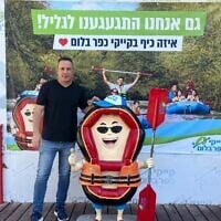 Eyal Greenwald, responsable marketing de Kfar Blum Kayaks, se tenant devant une pancarte sur laquelle on peut lire « La Galilée nous a manqué, à nous aussi ! », au kibboutz Kfar Blum, en Haute-Galilée, le 11 août 2026. (Crédit : Diana Bletter/Times of Israel)