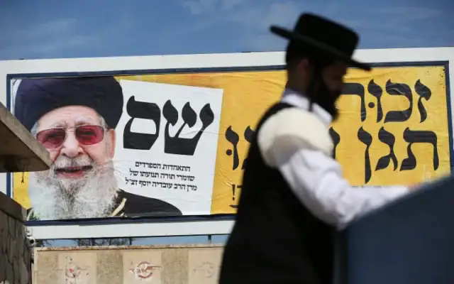 Un juif ultra-orthodoxe passe devant un panneau d'affichage présentant une photo du défunt chef spirituel du Shas, le rabbin Ovadia Yosef, dans le cadre de la campagne électorale du Shas, dans la ville de Safed, au nord d'Israël, le 28 février 2020. (Crédit: David Cohen/Flash90)