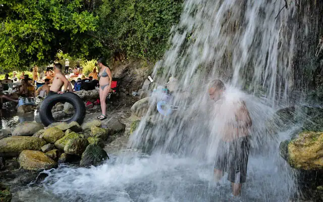 Des personnes profitant d'une cascade se jetant dans le lac de Tibériade, près de Kfar Nahum, dans le nord d'Israël, le 1ᵉʳ août 2026. (Crédit : Michael Giladi/Flash90)