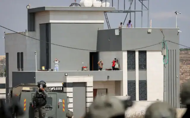 Des militants israéliens et des habitants palestiniens se tenant sur le toit d'une maison assiégée par des résidents d'implantations, dans le village de Qusra, au sud de Naplouse, en Cisjordanie, le 14 août 2026. (Crédit : Flash90)