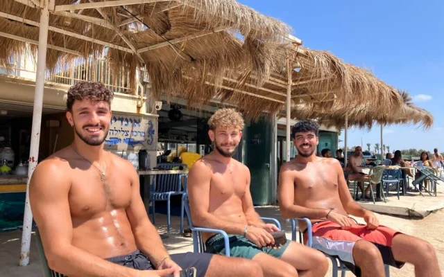 Nitzan Eliyahu, Shon Brener et Omer Maoz bronzent sur la plage de Shavei Zion, en Galilée occidentale, le 16 juillet 2026. (Diana Bletter/Times of Israel)
