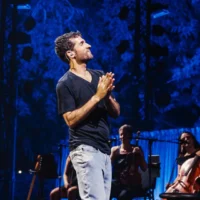 L'ancien otage Sagui Dekel-Chen interprétant les chansons qu'il a composées pendant sa captivité, sur la pelouse du kibboutz Nir Oz, dans le cadre du Festival d'Israël, le 10 août 2026. (Crédit : Orit Pnini)