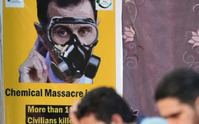 Des personnes sont assises face à une affiche représentant le président syrien Bachar al-Assad portant un masque à gaz, lors d'un événement organisé le 20 août 2023 dans la ville d'Afrin, au nord du pays, contrôlée par les rebelles, pour marquer le 10e anniversaire des attaques chimiques à  la Ghouta, près de la capitale. (Crédit: Rami al Sayed/AFP)