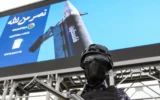Un agent de sécurité monte la garde devant une immense image représentant un missile sur lequel est inscrit "Palestine", lors d'un rassemblement organisé par des partisans du groupe terroriste Houthi, soutenu par l'Iran, en solidarité avec l'Iran et le Liban dans le contexte de la guerre au Moyen-Orient, à Sanaa, la capitale, le 17 avril 2026. (Crédit: Mohammed HUWAIS/AFP)
