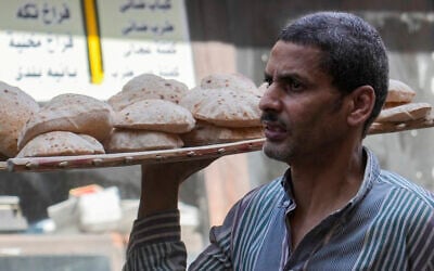 Un homme portant un plateau de pain sur un marché populaire du Caire, en Égypte, le 7 juin 2024. (Crédit :  Amr Nabil/AP)