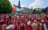 Des dizaines de milliers de manifestants vêtus de rouge défilant devant le Palais de la Paix, qui abrite la Cour internationale de justice (à l'arrière-plan), pour exiger de leur gouvernement qu'il prenne davantage de mesures afin de mettre un terme à l'offensive israélienne à Gaza, lors d'une manifestation à La Haye, aux Pays-Bas, le 15 juin 2025. (Crédit : Peter Dejong/AP)