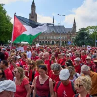 Des dizaines de milliers de manifestants vêtus de rouge défilant devant le Palais de la Paix, qui abrite la Cour internationale de justice (à l'arrière-plan), pour exiger de leur gouvernement qu'il prenne davantage de mesures afin de mettre un terme à l'offensive israélienne à Gaza, lors d'une manifestation à La Haye, aux Pays-Bas, le 15 juin 2025. (Crédit : Peter Dejong/AP)