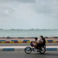 Deux hommes circulent à moto le long du littoral alors que des navires commerciaux sont ancrés dans le détroit d'Ormuz, au large de Bandar Abbas, en Iran, le 4 septembre 2026. (AP Photo/Vahid Salemi)