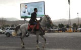 Un homme passe à cheval sous un panneau d'affichage montrant le chef houthi Abdul Malik al-Houthi accompagné d'une phrase du Coran, qui se lit en arabe : « C'est par la grâce d'Allah et par Sa miséricorde qu'ils se réjouissent ; c'est mieux que tout ce qu'ils accumulent », à Sanaa, au Yémen, le dimanche 6 septembre 2026. (Crédit :  AP/Osamah Abdulrahman)