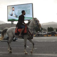 Un homme passe à cheval sous un panneau d'affichage montrant le chef houthi Abdul Malik al-Houthi accompagné d'une phrase du Coran, qui se lit en arabe : « C'est par la grâce d'Allah et par Sa miséricorde qu'ils se réjouissent ; c'est mieux que tout ce qu'ils accumulent », à Sanaa, au Yémen, le dimanche 6 septembre 2026. (Crédit :  AP/Osamah Abdulrahman)