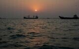 Le soleil se couchant sur des navires marchands ancrés dans le détroit d'Ormuz, au large de Bandar Abbas, en Iran, avec la silhouette de la ville en arrière-plan, le 6 septembre 2026. (Crédit : Vahid Salemi/AP)