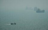 Un bateau à moteur passe dans la brume devant des navires marchands ancrés dans le détroit d'Ormuz, au large de Bandar Abbas, en Iran, le 7 septembre 2026. (Crédit : AP Photo/Vahid Salemi)