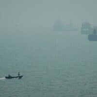 Un bateau à moteur passe dans la brume devant des navires marchands ancrés dans le détroit d'Ormuz, au large de Bandar Abbas, en Iran, le 7 septembre 2026. (Crédit : AP Photo/Vahid Salemi)