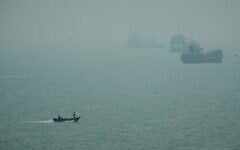 Un bateau à moteur passant devant des navires commerciaux ancrés dans la brume dans le détroit d'Ormuz, au large de Bandar Abbas, en Iran, le 7 septembre 2026. (Crédit : Vahid Salemi/AP)