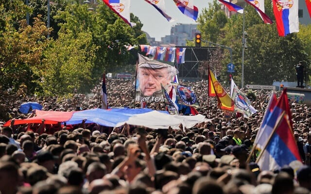 Des personnes rassemblées pour le cortège funèbre brandissent un drapeau à l'effigie de l'ancien commandant de l'armée serbe de Bosnie, Ratko Mladić, décédé la semaine dernière alors qu'il purgeait une peine de prison à perpétuité pour génocide et autres atrocités commises pendant la guerre en Bosnie, à l'issue d'un office religieux à l'église Saint-Luka, à Belgrade, en Serbie, le 7 septembre 2026. (Crédit : Darko Vojinovic/AP)