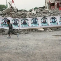 Un enfant courant devant une banderole tendue au-dessus des décombres de l'école Shajareh Tayyebeh, sur laquelle figurent les portraits des enfants et des enseignants tués lors d'une frappe aérienne américaine le 28 février à Minab, dans le sud de l'Iran, le 7 septembre 2026. (Crédit : Vahid Salemi/AP)
