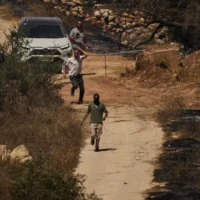 Des résidents d’implantations israéliennes, dont certains sont masqués, courent le long d’une route pour empêcher des Palestiniens de la région d’y accéder, à la suite d’une attaque au cours de laquelle des résidents d’implantations auraient, selon les habitants, mis le feu à la zone, dans le village de Burqa, en Cisjordanie, le 17 septembre 2026. (Crédit : Leo Correa/AP)