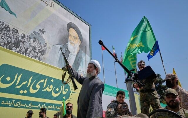 Un religieux chiite armé passe à bord d'un véhicule militaire devant un panneau d'affichage représentant l'ayatollah Ruhollah Khomeini, fondateur de la République islamique, lors du défilé militaire dit « Janfada », ou « Sacrifice pour l'Iran », organisé par l'État à Téhéran, en Iran, le 18 septembre 2026. (Crédit : AP Photo/Vahid Salemi)