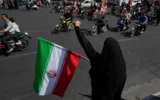 Une femme scande des slogans en brandissant un drapeau iranien tandis que des motards défilent lors d'un défilé organisé par l'État, appelé "Janfada", qui signifie "Sacrifice pour l'Iran", à Téhéran, en Iran, le 25 septembre 2026. (Crédit: AP/Vahid Salemi)