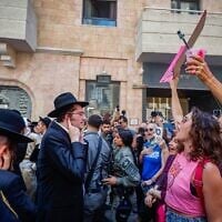 Des hommes haredim manifestent devant le Café Basimta pour dénoncer son ouverture à Shabbat, tandis que des contre-manifestants laïques se tiennent face à eux, à Jérusalem, le 8 août 2026. (Crédit : Oren Ben Hakoon/Flash90)