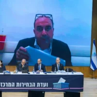 Le chef du parti Balad, Sami Abou Shahdeh, apparaissant sur un écran derrière la commission centrale électorale lors d'une audience relative à une demande d'inéligibilité à la Knesset, à Jérusalem, le 23 septembre 2026. (Crédit : Yonatan Sindel/Flash90)