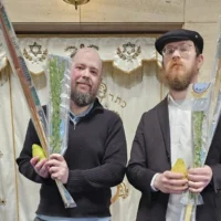 Daniel Rosenbaum (à gauche) et le rabbin Elchanan Kuperman tenant des ensembles des « quatre espèces » devant l'arche de la synagogue du Centre communautaire juif de Wellington, à Wellington, en Nouvelle-Zélande, le 22 septembre 2026. (Crédit : Daniel Rosenbaum)