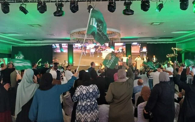 Des partisans de Raam agitent le drapeau vert du parti en regardant les sondages de sortie des urnes au siège du parti à Sakhnin, le 27 octobre 2026. (Noam Lehmann/Times of Israel) Des partisans de Raam agitent le drapeau vert du parti en regardant les sondages de sortie des urnes au siège du parti à Sakhnin, le 27 octobre 2026. (Noam Lehmann/Times of Israel)