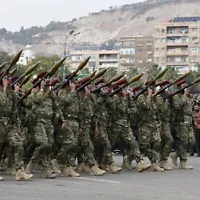 Des personnes agitant des drapeaux syriens alors qu’elles assistent à un défilé militaire célébrant le premier anniversaire de la chute de Bachar al-Assad, dictateur de longue date, à Damas, le 8 décembre 2025. (Crédit : Louai Beshara/AFP)