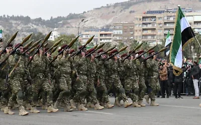 Des personnes agitant des drapeaux syriens alors qu’elles assistent à un défilé militaire célébrant le premier anniversaire de la chute de Bachar al-Assad, dictateur de longue date, à Damas, le 8 décembre 2025. (Crédit : Louai Beshara/AFP)