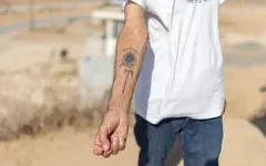 Danny, un habitant du kibboutz Nahal Oz, montrant le tatouage à l'encre noire représentant un tournesol qu'il porte sur l'avant-bras, accompagné d'une inscription en hébreu signifiant « Le chemin vers l'espoir », qu'il s'est fait faire en mémoire du pogrom perpétré par le groupe terroriste palestinien du Hamas le 7 octobre 2023, à Nahal Oz, dans le sud d'Israël, le 22 octobre 2026. (Crédit : Ilia Yefimovich/AFP)